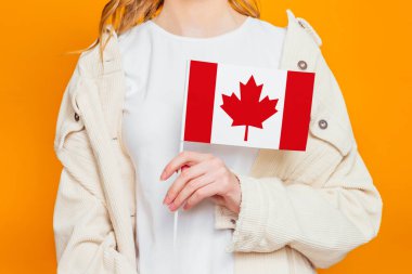 Kanada bayrağını tutan kadın el turuncu arka planda izole edilmiş, Kanada Günü kutlaması. Kanada bayrağı kızın elinde.