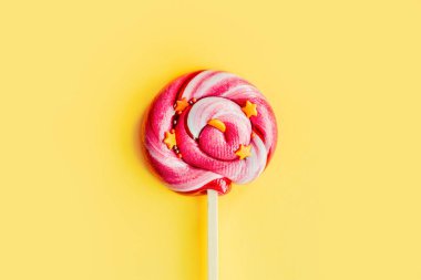 Sarı kağıttan izole edilmiş renkli pembe lolipop. Düz yatıyordu. Uzayı kopyala Minimum konsept. Kapat.