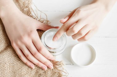 Beyaz arka planda krema kavanozu olan bir kadın eli. Kız ellerine nemlendirici sürüyor. Kuru çiçek yaprakları, üst manzara. Ekolojik, doğal parfümsüz krem, doğal el bakımı yağı..