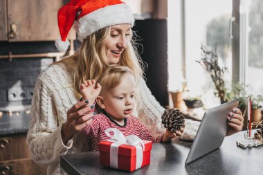 Yeni yıl videoları. Yeni yıl şapkası takmış bir anne oğluyla mutfakta oturmuş video görüşmeleri yapıyor. Aile, Coronavirus karantinası sırasında yeni yılı kutluyor.