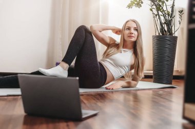 Kafkasyalı sarışın kız evde defter ile yoga egzersizi yapıyor. Karantina sırasında yoga dersleri. Pandemik karantina sırasında sağlıklı yaşam tarzı