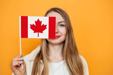 Kafkas öğrenci kız yüzünün yarısını Kanada bayrağıyla kaplamış ve mavi arkaplanda izole edilmiş bir kamera arıyor. Kanada günü, tatil günü, konfederasyon yıldönümü, kopyalama alanı.
