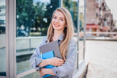 Kafkasyalı mutlu kız öğrenci elinde defter klasörleri ile şehrin sokaklarında yürür.
