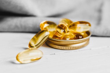 Sarı kapsüller, tabletler, balık yağı hapları beyaz ahşap bir masada yatıyor. Vitamin kompleksi Omega 3,6,9.