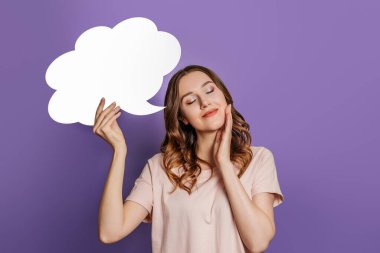 Öğrenci kız gözleri kapalı ve mor arka planda izole edilmiş boş bir konuşma balonu tutuyor. Boşluğu kopyala