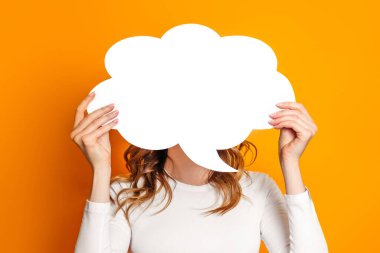 Elinde boş konuşma balonu kağıdı tutan kadın turuncu arka planda izole edilmiş. Sarı arkaplan üzerine beyaz kağıt bulutu. Boşluğu kopyala