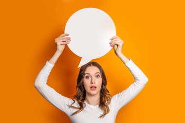 Genç şok olmuş kız öğrenci elinde kağıt konuşma balonu kağıdıyla turuncu arka planda izole edilmiş. Sarı arkaplan üzerine beyaz kağıt bulutu. Boşluğu kopyala