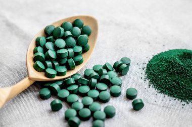 Tabletlerde yeşil yosun spirulinası ve gri arka planda toz. Sağlıklı sebze proteini. Süper yemek.