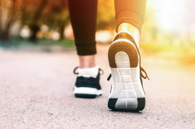 Sabah koşusu. Kırsal bir yolda koşan genç bayan gün batımında siyah spor ayakkabılarıyla beyaz tabanlı.