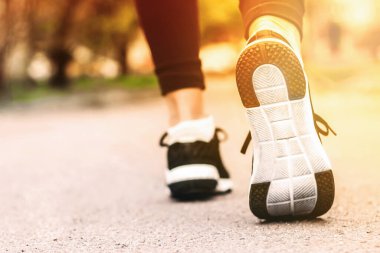 Sabah koşusu. Kırsal bir yolda koşan genç bayan gün batımında siyah spor ayakkabılarıyla beyaz tabanlı.