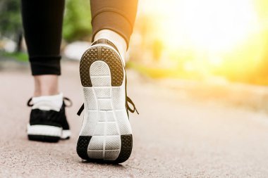 Sabah koşusu. Kırsal bir yolda koşan genç bayan gün batımında siyah spor ayakkabılarıyla beyaz tabanlı.