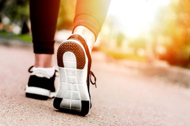 Sabah koşusu. Kırsal bir yolda koşan genç bayan gün batımında siyah spor ayakkabılarıyla beyaz tabanlı.