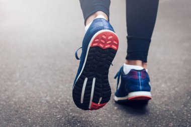 Sabah koşusu. Kırsal bir yolda koşan genç bayan gün batımında siyah tabanlı mavi spor ayakkabılarla koşuyor. Sağlıklı bir yaşam tarzı. Spor eğitimi konsepti