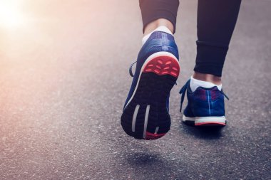 Sabah koşusu. Kırsal bir yolda koşan genç bayan gün batımında siyah tabanlı mavi spor ayakkabılarla koşuyor. Sağlıklı bir yaşam tarzı. Spor eğitimi konsepti