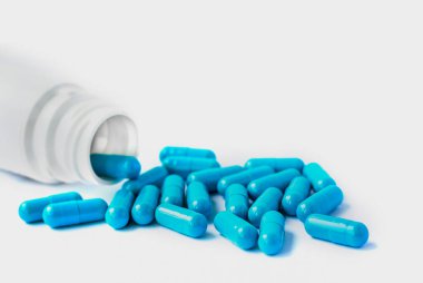 Mavi kapsüller, beyaz arka planda izole edilmiş haplar ve fotokopi alanı. Beyaz kavanozdaki kapsüller. Vitaminler, kadın sağlığı için besin takviyeleri