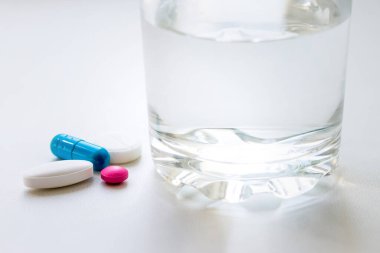 Su toplayan haplar, kapsüller, beyaz arka planda bir bardak su. Soğuk algınlığı, vitamin ve sağlık kompleksinin tedavisi için hazırlıklar
