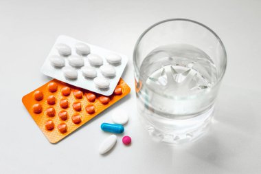 Su toplayan haplar, kapsüller, beyaz arka planda bir bardak su. Soğuk algınlığı, vitamin ve sağlık kompleksinin tedavisi için hazırlıklar