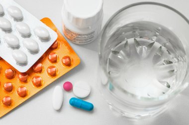 Su toplayan haplar, kapsüller, beyaz arka planda bir bardak su. Soğuk algınlığı, vitamin ve sağlık kompleksinin tedavisi için hazırlıklar