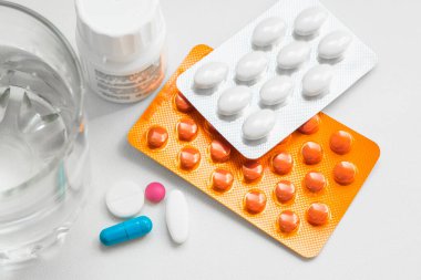 Su toplayan haplar, kapsüller, beyaz arka planda bir bardak su. Soğuk algınlığı, vitamin ve sağlık kompleksinin tedavisi için hazırlıklar