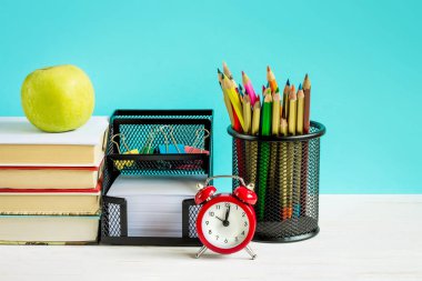 Okul konseptine geri dönelim. Kırmızı alarm, elma, renkli kalemler, mavi arka planda kitaplar. 1 Eylül konsepti.