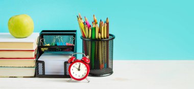 Okul konseptine geri dönelim. Kırmızı alarm, elma, renkli kalemler, mavi arka planda kitaplar. 1 Eylül konsepti, kopya alanı olan okul pankartı