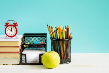 Okul konseptine geri dönelim. Kırmızı alarm, elma, renkli kalemler, mavi arka planda kitaplar. 1 Eylül konsepti.