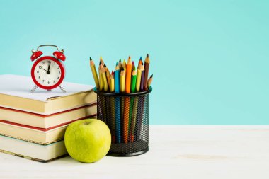 Okul konseptine geri dönelim. Kırmızı alarm, elma, renkli kalemler, mavi arka planda kitaplar. 1 Eylül konsepti.