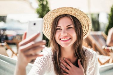 Yazın plajda hasır şapkayla oturan kız çok utanmış ve gülümsüyor.