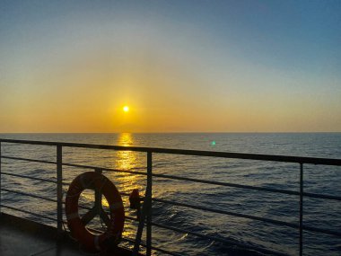 Yaz gezisi konsepti. Ufkun üzerinde güzel bir günbatımı olan panoramik deniz manzarası. Sakin denize güneş yansıması. Bir yolcu gemisinin güvertesinden gün batımı.