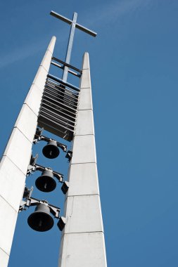 Arka planda mavi gökyüzü olan modern kilise çan kulesi. Tepesinde haç olan üç çan. Piestany, Slovakya. Dini tema.