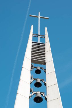 Arka planda mavi gökyüzü olan modern kilise çan kulesi. Tepesinde haç olan üç çan. Piestany, Slovakya. Dini tema.