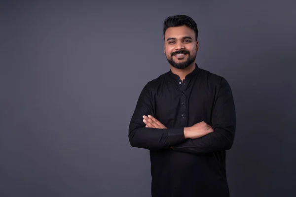 Happy smiling man looking at camera. Pakistani young man in traditional black shirt clothes. Man with dark hair, mustache beard. arms crossed.