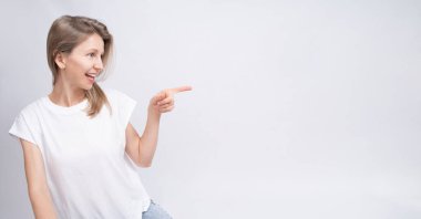 Sarışın kadın profili, uzun saçlı, yan tarafı gösterişli, sakin bir gülümsemesi var. Uzun yatay arkaplan. Beyaz tişört ve gri arka plan