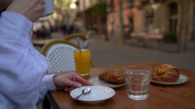 Sabah kahvaltısı, kahve, kruvasan ve portakal suyu. Barcelona 'daki sokak kafesi. Video görüntüleri. Dışarıdaki masada oturan bir kadın.