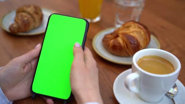 带有绿色铬色屏的手机手握着垂直的肖像位置 手刷左右手 街边咖啡馆早餐 咖啡和羊角面包 模板视频画面空白复制空间 — 图库视频影像