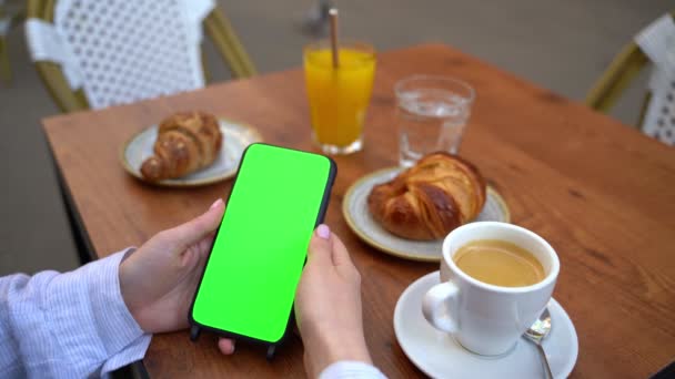 手拿着绿色铬钥匙的手机 禁止使用社交媒体触摸屏观看在线电影交流 街头咖啡馆休息与咖啡和羊角面包 模板视频镜头 — 图库视频影像