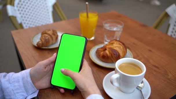 滚动社交媒体的新闻手拿着绿色屏幕的铬钥匙手机 街上的咖啡店 咖啡和羊角面包 模板视频镜头4K — 图库视频影像