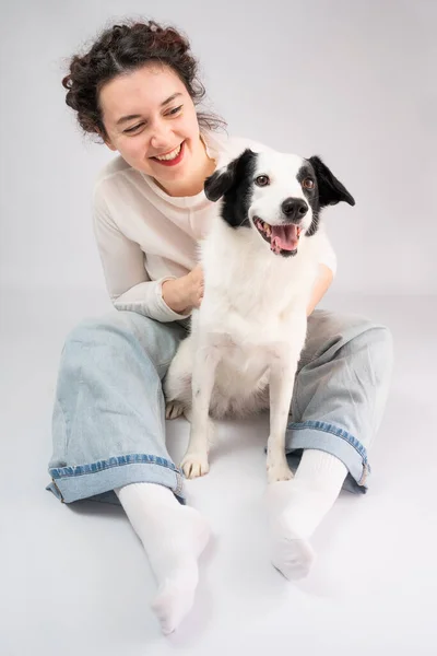 Gri Arka Planda Oturan Köpek Kadın Gülümsüyor Kot Pantolonlu Beyaz — Stok fotoğraf