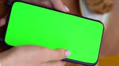 Yeşil renkli ekranlı telefonu tutan elleri sola kaydırın ve sağa kaydırın. Cep telefonuyla film izleyen ya da sosyal medyada haber yayınlayan bir kadın. Dikey olarak video görüntülerini kapat.