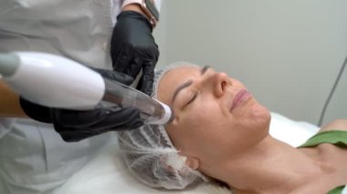 Yaşlanma önleyici kozmetik prosedürü Transdermal Mezoterapi ürün serumu güçlü hava basıncının etkisiyle deriye nüfuz eder. Güzellik uzmanının ofisindeki video görüntüleri. Sakin sabırlı kadın.