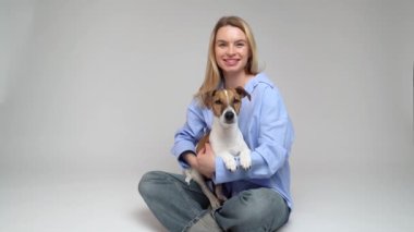 Sevimli köpek Jack Russell Terrier 'ı tutan gülen sarışın kadın. Bakım ve sevgi köpek sahibi. Stüdyo video görüntüleri