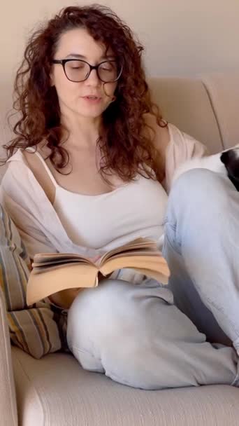 Χαμογελώντας Σγουρά Μαλλιά Γυναίκα Γυαλιά Διαβάζοντας Βιβλίο Κάθεται Στον Καναπέ — Αρχείο Βίντεο