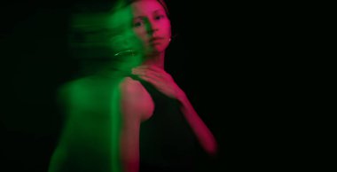 Siyah arka plandaki kadın kameraya bakıp boynuna dokunarak rahatladı. Huysuz, rüya gibi, sakin, uzun pozlama fotoğrafçılığı. Yaratıcı kavramsal görüntü. Yeşil ve kırmızı. Dinamik sanatsal portre