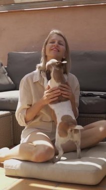 Köpek, güneş terasında oturan sarışını öpüyor. Mutlu bir şekilde kuyruğunu sallıyor. Zevk aşkı ve dostluğun güveni. Hafta sonu evcil hayvanımızla takılacağız. Dikey video görüntüleri