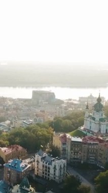Hava kameraları St. Andrew Kilisesi ve St. Andrew 's Descent' in üzerinden Podil ve Dnipro Nehri 'ne doğru uçuyor. Gün doğumu yumuşak yaz arkaplanı. Dikey video görüntüleri 