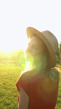 Hasır şapkalı kadın kameraya bakıyor ve gülümsüyor. Sarı saçlı ve kırmızı elbiseli. Güneşli yaz havası dikey video görüntüleri. Tatil gevşemiş ruh hali