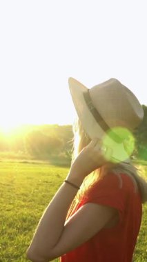 Hasır şapkalı genç sarışın kadın gözleri kapalı rahatlamış gülümsüyor. rüya gibi yaz güneşli dikey video