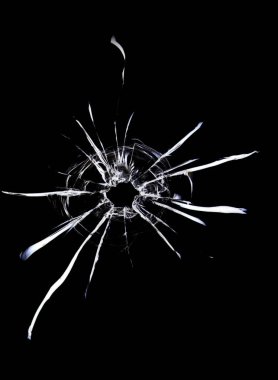 Cracks in the glass on a black background. A bullet hole in a window on a dark background.