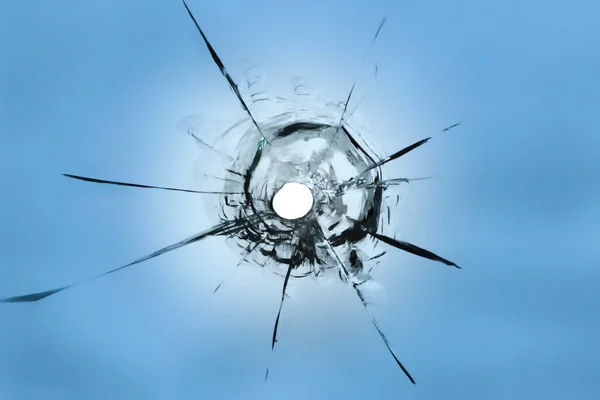 stock image A hole from a weapon hitting the glass. Cracked window on a blue background