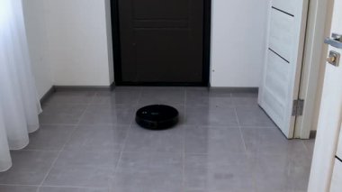 Siyah robot elektrikli süpürge modern bir dairede gri fayanslı zemini temizliyor.